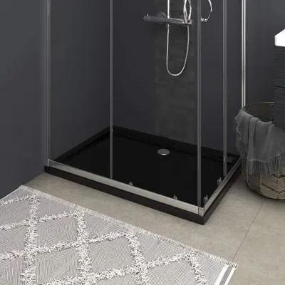 A close-up view of a black rectangular shower tray with a silver trim, placed on a tiled floor next to a grey and white patterned rug.