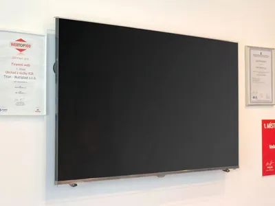A large, flat-screen television is mounted on a white wall, with several framed certificates or awards displayed to its left and right.