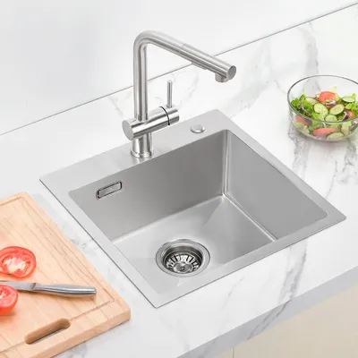 A stainless steel kitchen sink with a faucet, a cutting board with tomatoes, and a bowl of salad on a marble countertop.