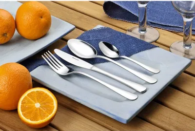 Cutlery set on a plate with oranges on a wooden table.