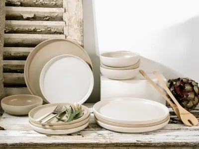 A collection of stoneware dinnerware, including plates and bowls, arranged on a rustic wooden surface.
