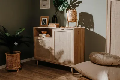A wooden sideboard with cane detailing in a room with green walls and wooden flooring.