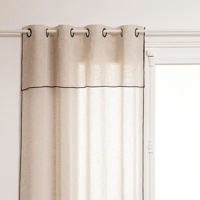 A close-up view of a beige curtain with black trim, hanging from a white curtain rod.