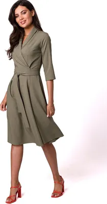 A woman wearing a dress and high heels, posing against a white background.