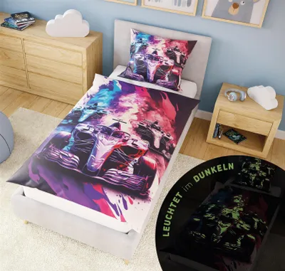 A child's bed with bedding featuring a racing car theme, with a nightstand and dresser in the background.