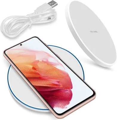 A smartphone is placed on a white wireless charger, with a white USB cable in the background.