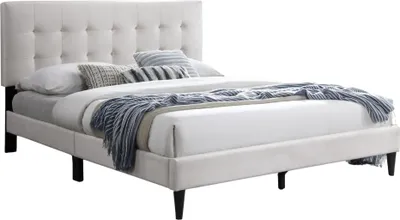 A beige upholstered bed with a tufted headboard and bedding.