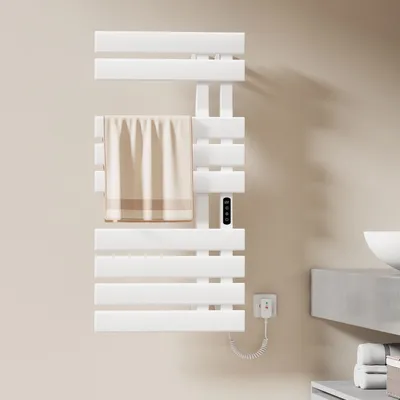 A white electric towel warmer mounted on a light-colored wall, with a beige towel draped over one of its bars. A power cord and plug are visible near the bottom.