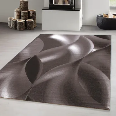 A modern, abstract design rug is shown on a light gray floor, with a fireplace and firewood in the background.