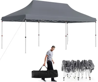 A man is carrying a folded tent in a bag next to a set-up tent.