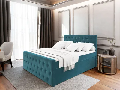 A bedroom scene featuring a teal upholstered bed with white bedding and pillows, a chair, and a side table.