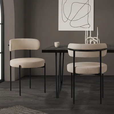 Two beige upholstered chairs with black metal legs are placed around a dark dining table in a modern room setting.