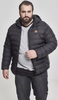 A man wearing a black puffer jacket and jeans against a light gray background.