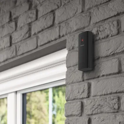 A black weather station mounted on a gray brick wall next to a window.