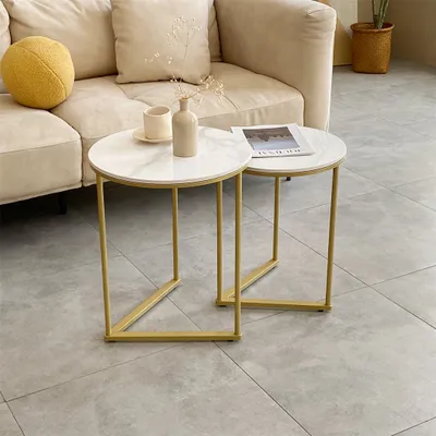 A set of two round nesting coffee tables with marble-look tops and gold metal frames, placed in a living room setting next to a sofa.