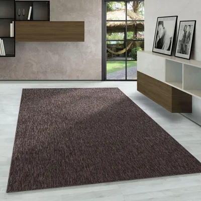 A modern living room with a rug, shelving unit, and a large window overlooking a garden.