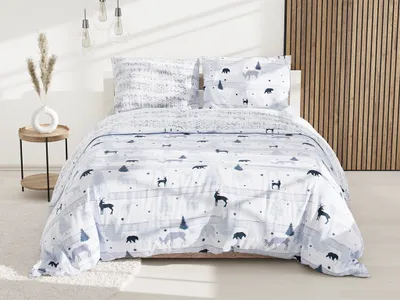 A neatly made bed with a white duvet cover featuring a pattern of deer, bears, and trees, set in a bedroom with a wooden accent wall and a side table with a vase of dried flowers.