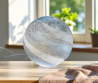 A glass sphere lamp sits on a wooden table in front of a window with plants.