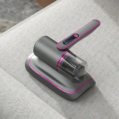 A handheld vacuum cleaner with a charging base is placed on a light gray fabric surface, possibly a sofa or mattress.