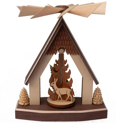 Ein hölzernes Pyramidenhaus zeigt einen Hirsch vor einem stilisierten Baum mit einem sich drehenden Flügelrad auf dem Dach und zwei kleinen Tannenbäumen an den Seiten