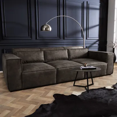 A dark gray microfiber sofa is shown in a living room setting with a dark blue paneled wall and a herringbone wooden floor.