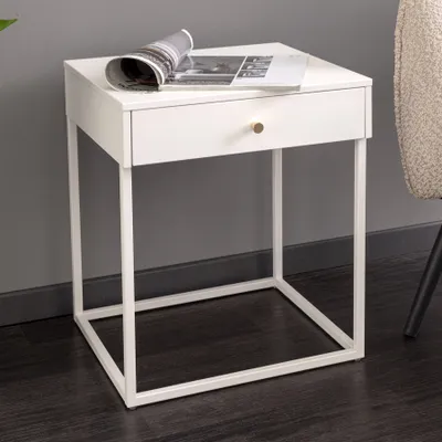 A white side table with a gold drawer knob is shown in a room with a dark floor and gray wall.
