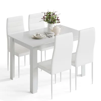 A white dining table with four white chairs, set with a plate, cutlery, a teapot, and a vase of flowers.