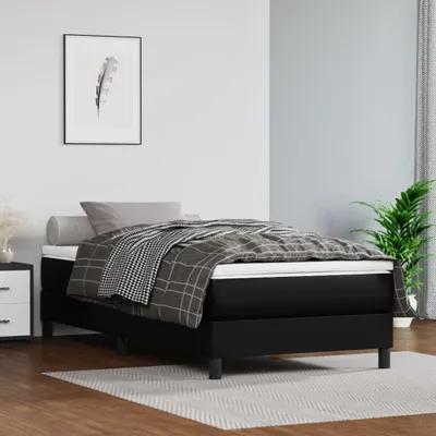 A bedroom scene with a black boxspring bed, bedding, and a framed picture on the wall.