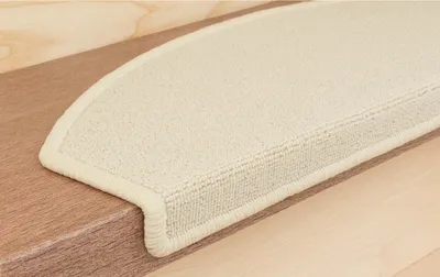 A close-up view of a beige carpet stair tread on a wooden step.