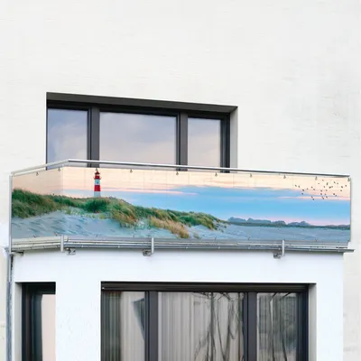 A balcony screen with a beach and lighthouse pattern is attached to a white building.