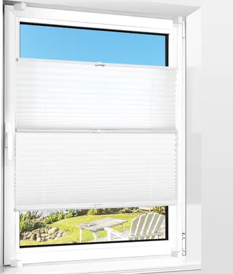 A white pleated blind is shown installed on a window, with a view of a garden and patio furniture visible through the lower section of the window.