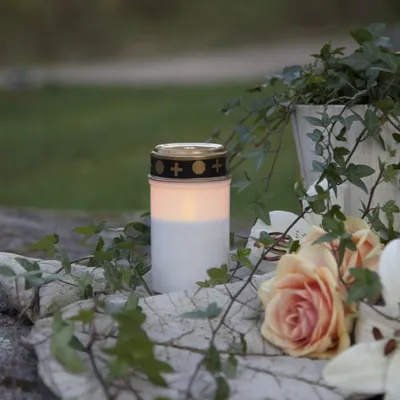A lit LED candle sits on a stone surface surrounded by ivy and roses.