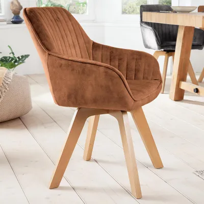 A brown velvet dining chair with wooden legs is shown in a well-lit room with wooden floors and a window in the background.