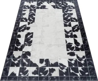 A rectangular rug with a patchwork design of black and white cowhide patterns, laid out on a white surface.
