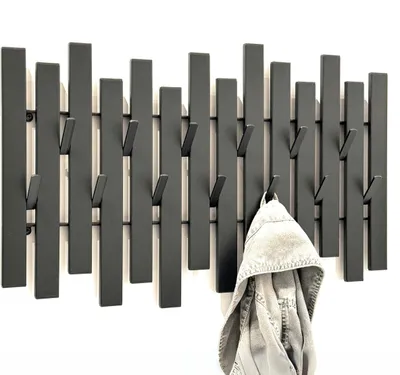 A black metal wall-mounted coat rack with multiple hooks against a white background. A grey jacket is hanging on one of the hooks.