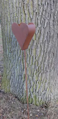 A rusty metal heart garden stake is placed next to a tree trunk.