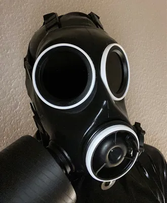 A close-up of a black gas mask with white rings around the eye lenses and the filter attachment.