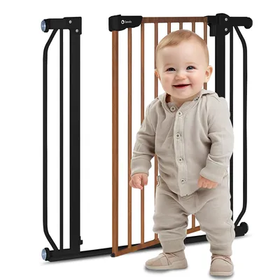 A baby is standing in front of a baby gate.
