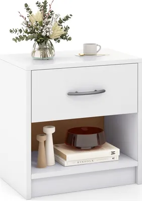 A white nightstand with a drawer and an open shelf, decorated with a vase of flowers and a coffee cup on top, and books and decorative items on the shelf.