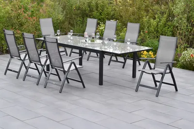 An outdoor dining set with a table and chairs on a patio, surrounded by greenery.