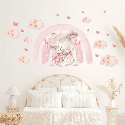 A nursery wall decorated with watercolor decals of bunnies, a rainbow, clouds, and hearts above a bed.