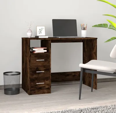 A dark wood desk with drawers and an open shelf, a laptop and office supplies on top, and a trash can to the side.