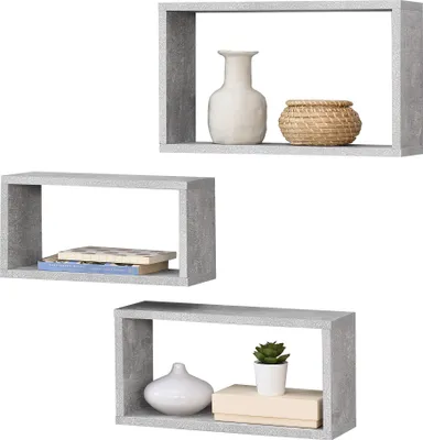 Three grey cube-shaped shelves are displayed against a white background. The top shelf contains a white vase and a woven basket. The middle shelf holds two books. The bottom shelf displays a white vase, a stack of two books, and a small potted plant.