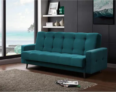 A teal sofa is placed in a living room with a large window overlooking the ocean.