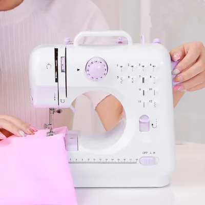 A person is using a white and purple sewing machine to sew a pink fabric.