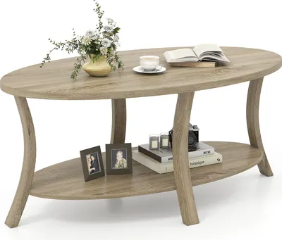 An oval-shaped coffee table with a lower shelf, decorated with a vase of flowers, a cup of coffee, a book, picture frames, and a camera.