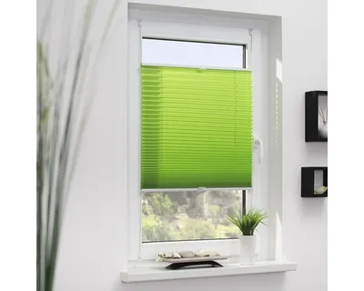 A green pleated blind is installed on a window, with a view of greenery outside.