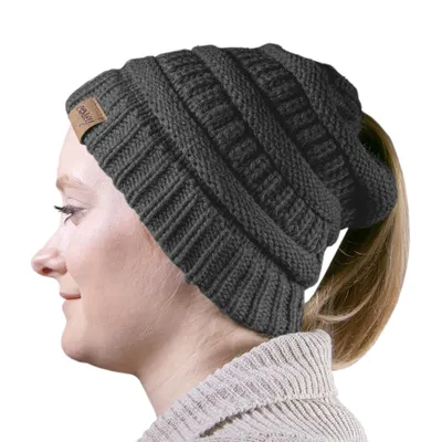 A woman wearing a dark gray knit beanie with a ponytail hole.