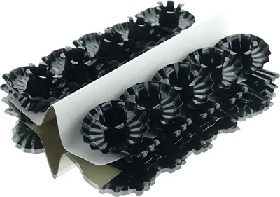 A stack of black candle holders with fluted edges, arranged in rows and separated by a white cardboard divider.