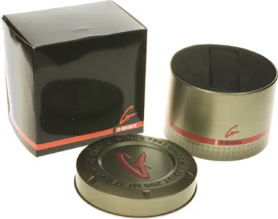 The image shows the packaging for a Casio G-Shock watch, including a black box and a cylindrical metal tin.